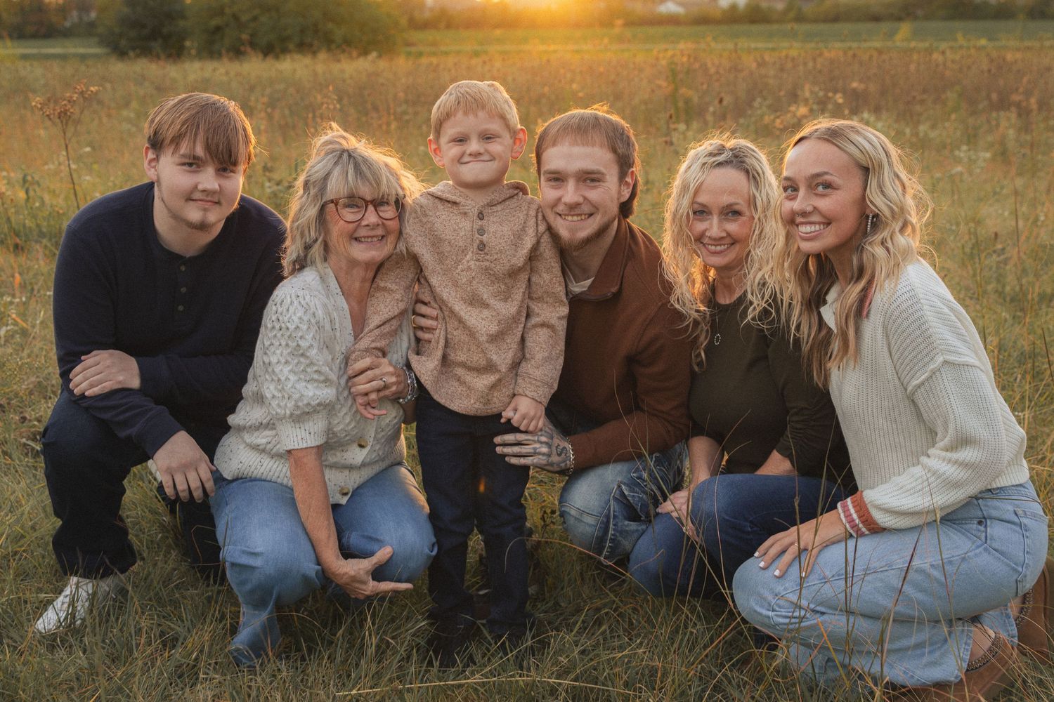 family gather on grass during golden hour for casual outdoor group photo.