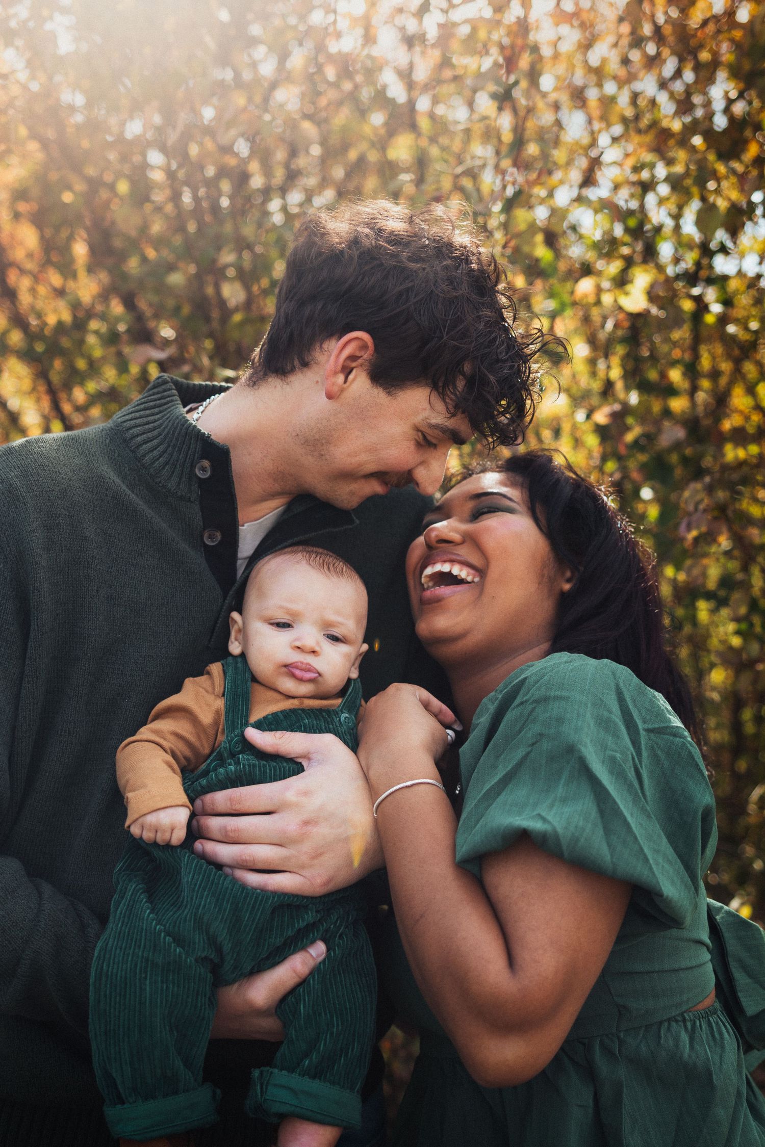 Tender family moment captured outdoors with golden sunlight filtering through autumn trees.
