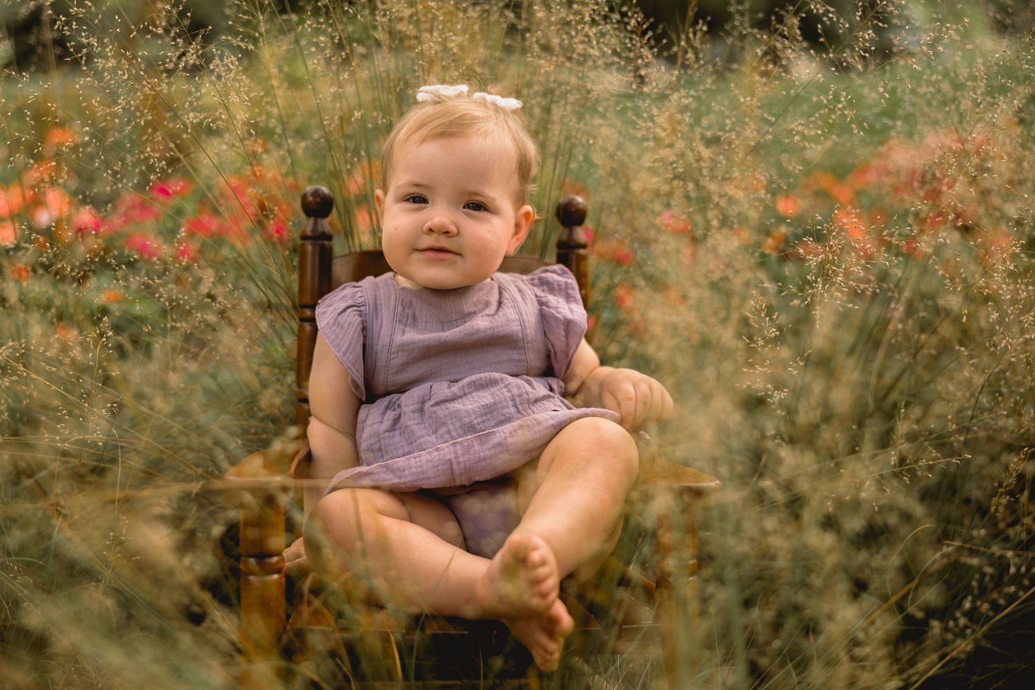 A child in purple clothing sits among wildflowers in a meadow.