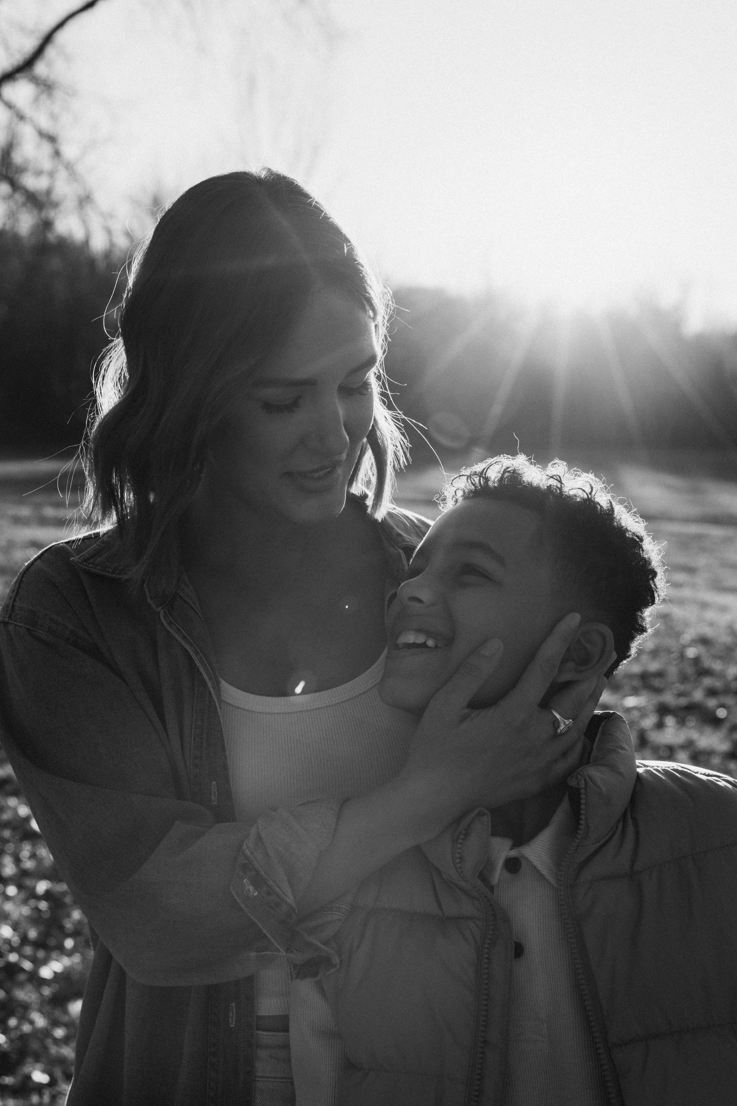 Black and white portrait of tender family moments backlit by setting sun.