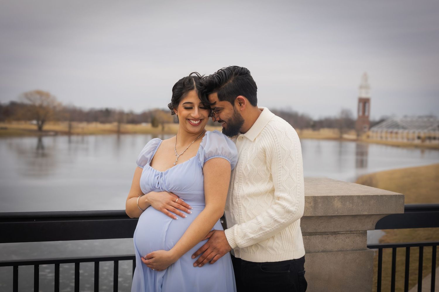 Romantic maternity photos taken by waterfront with city skyline in background.