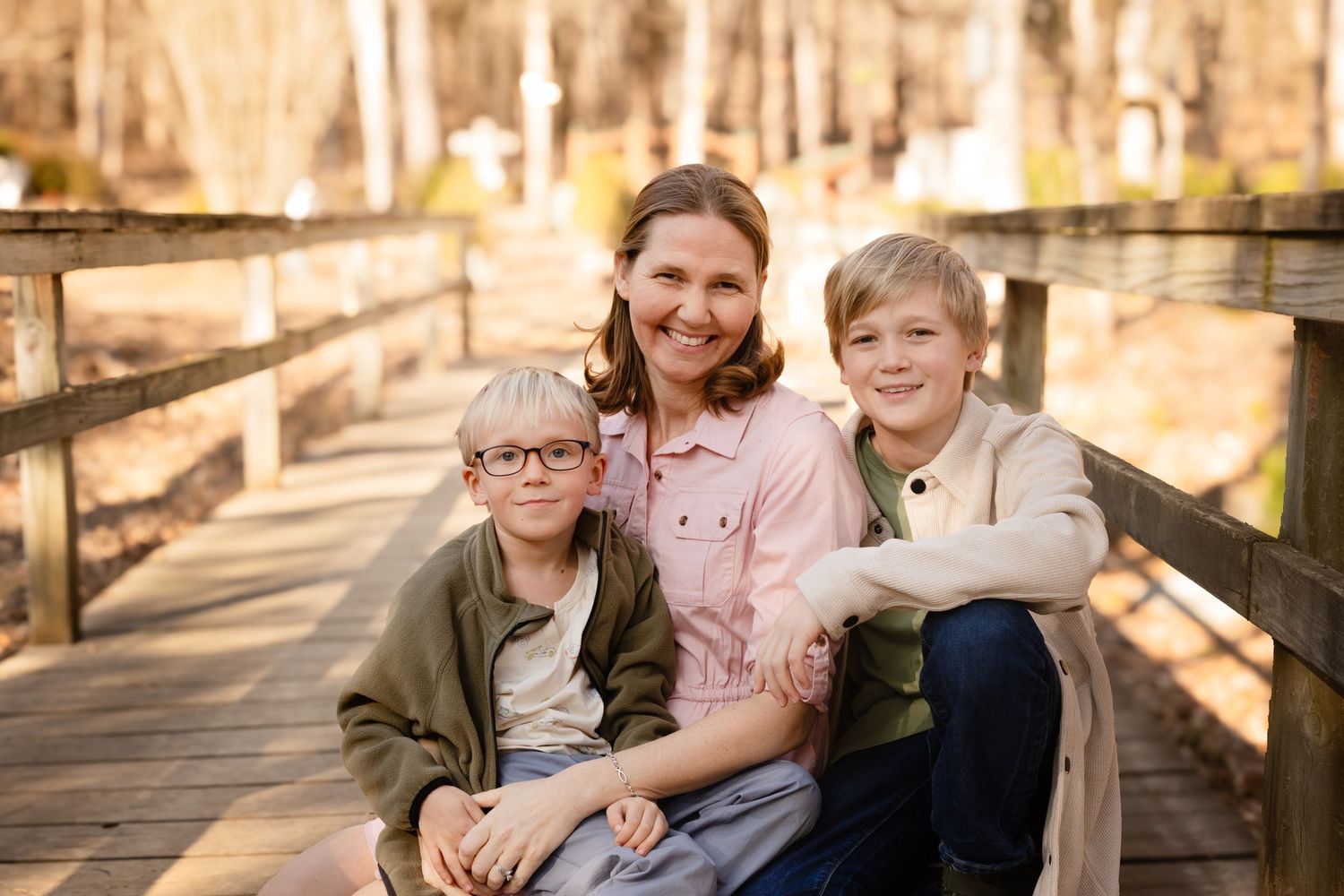 Family group sitting together on wooden boardwalk in autumn woods.