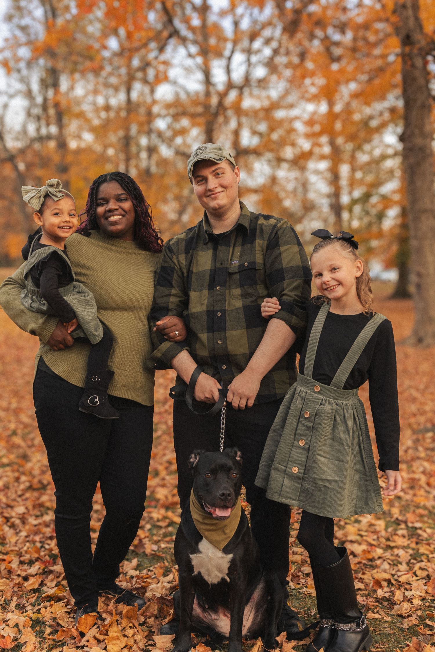 Family with dog posing together in fallen autumn leaves wearing coordinated outfits.