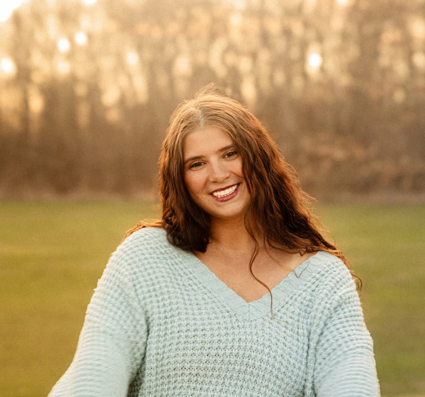 Person in mint sweater smiling during outdoor sunset photoshoot.
