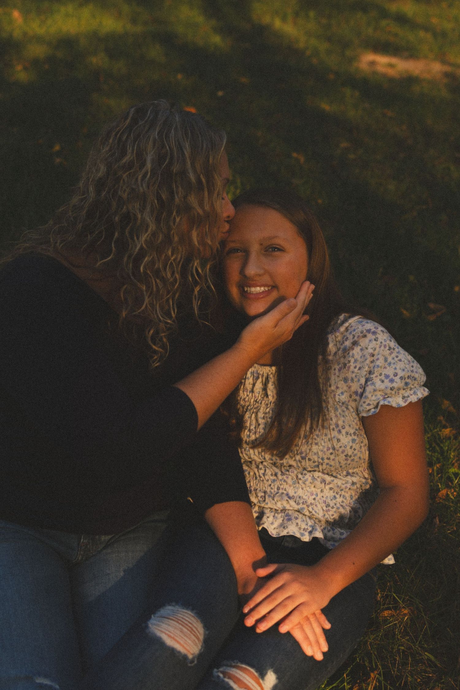 Two people sharing an intimate moment while sitting on grass in golden sunlight.