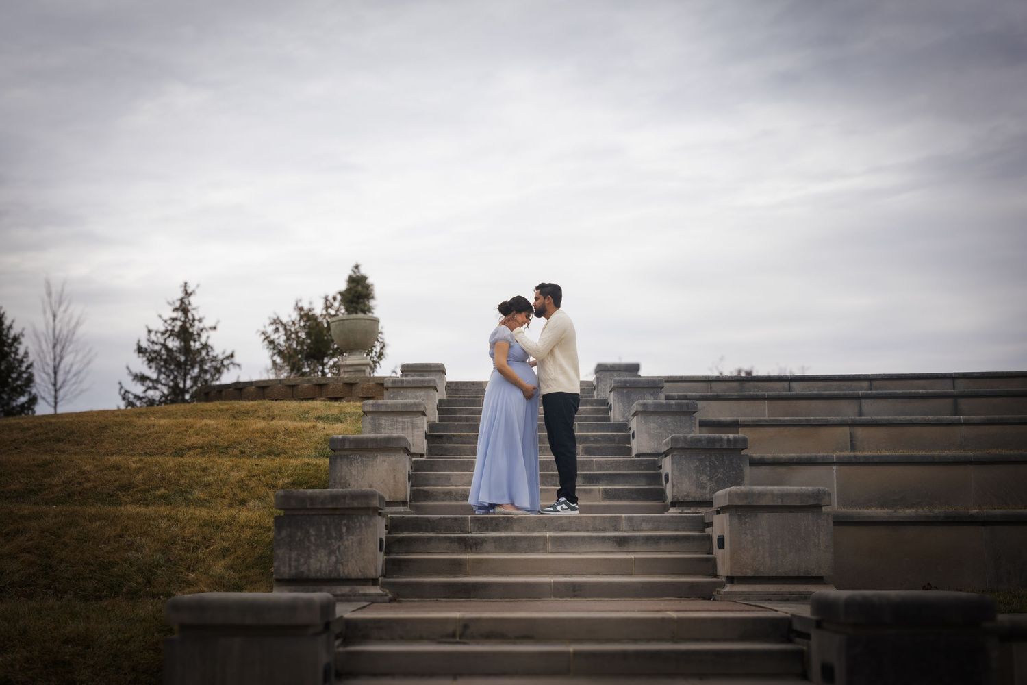 Couple poses on concrete amphitheater steps during cloudy day photoshoot.