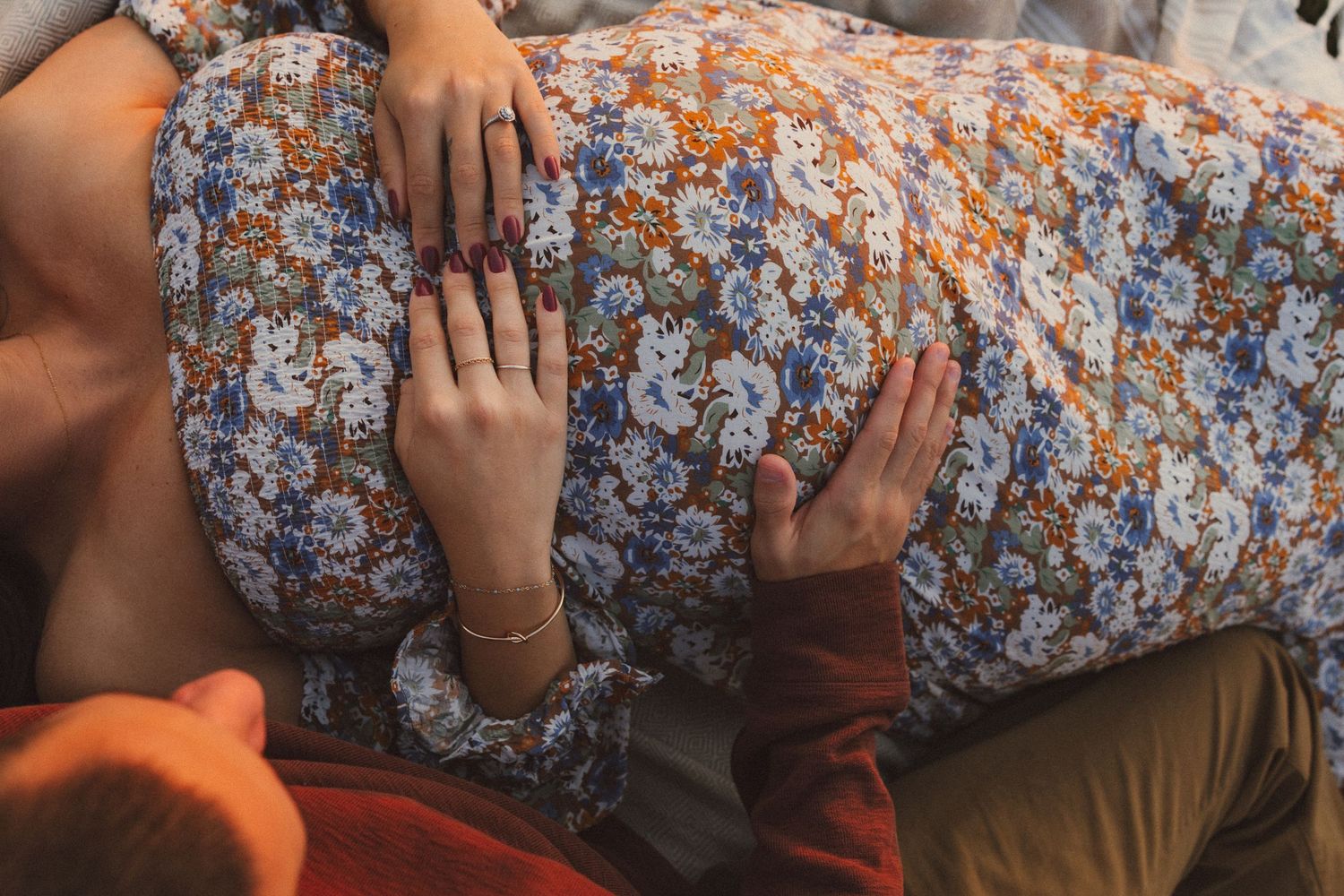 Close-up view of floral dress fabric and hands resting on stomach.