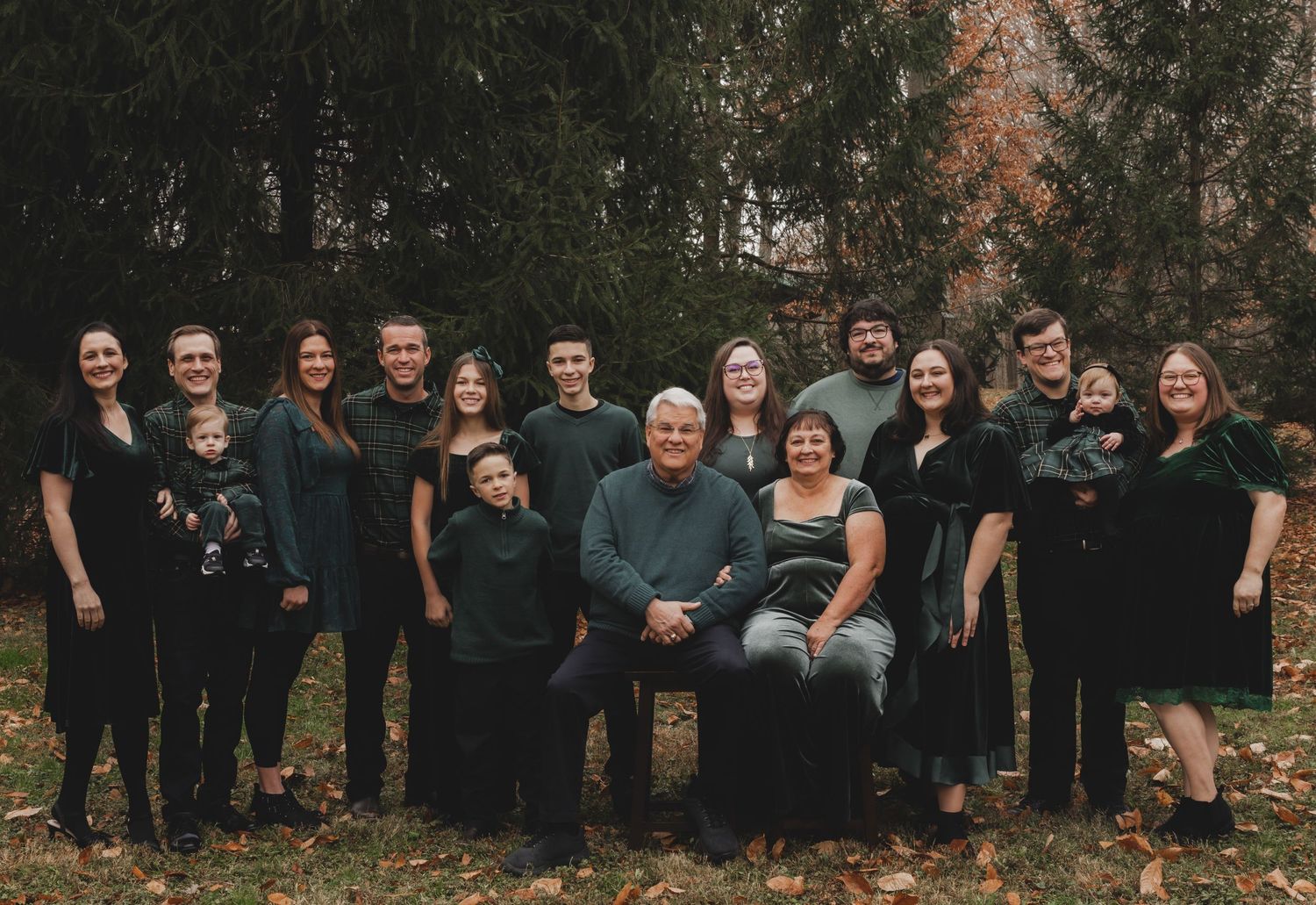 Large extended family poses together in coordinated dark outfits for outdoor group photo.