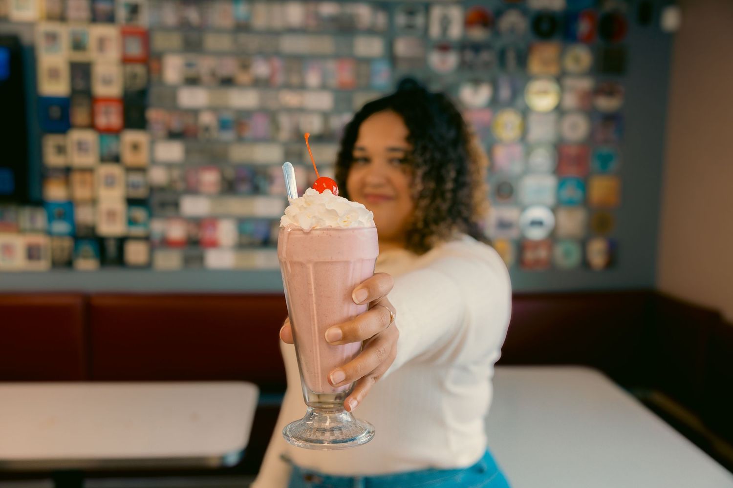 Person holding pink milkshake in retro diner setting.