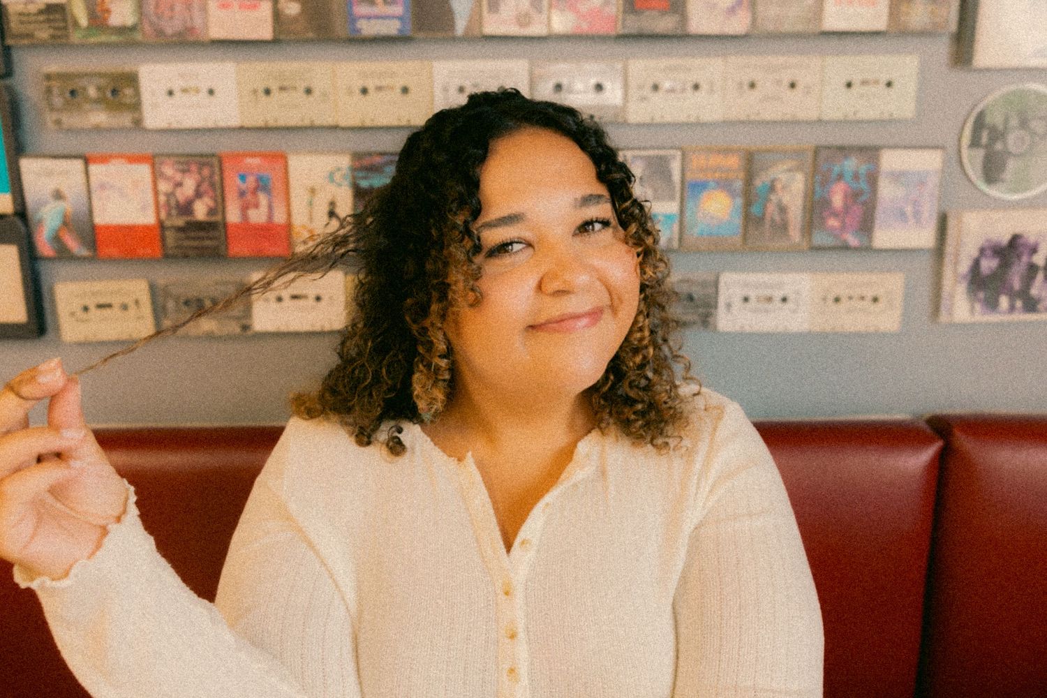 Person in white cardigan smiling while seated in retro diner with vintage decor.