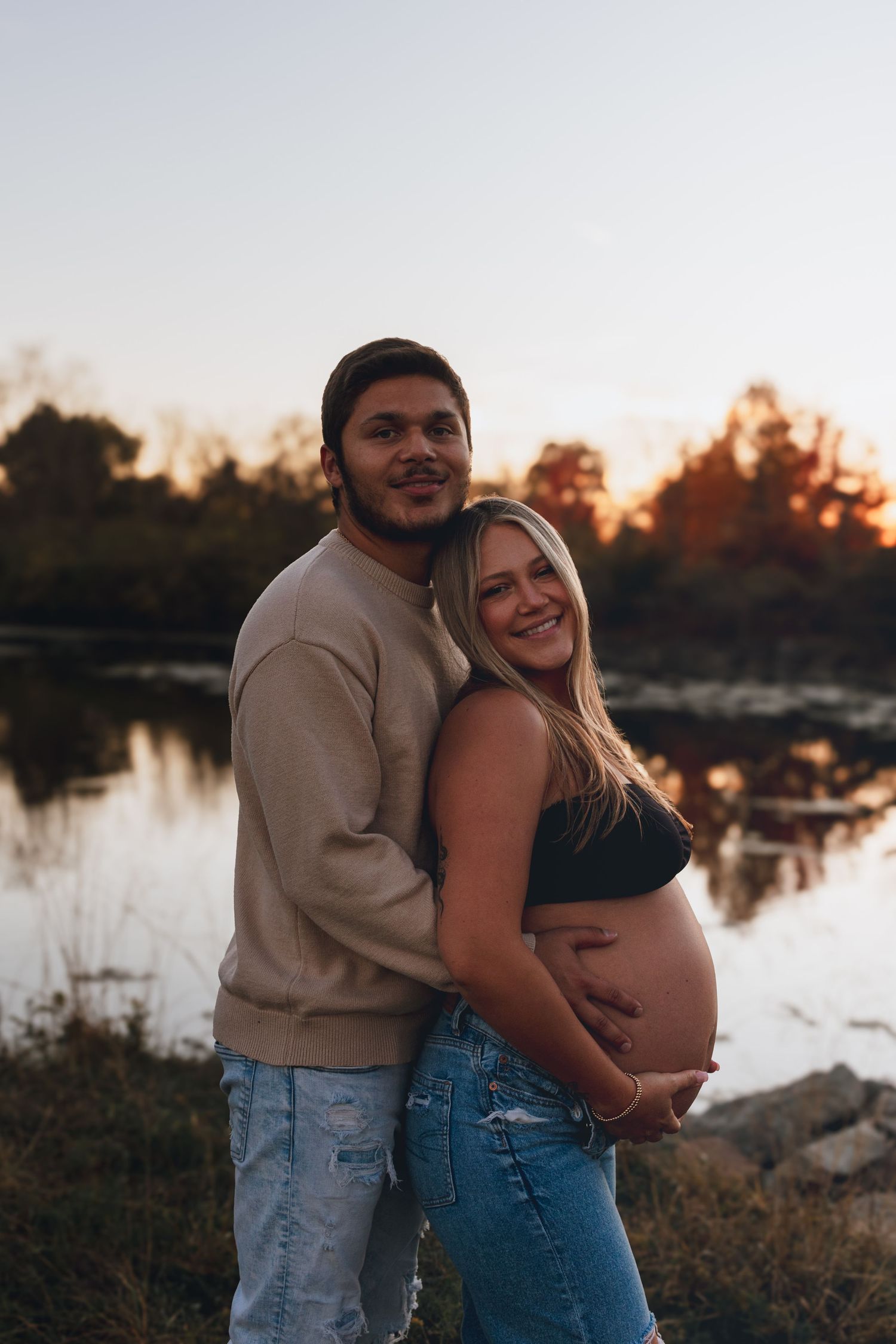 A couple embraces near a peaceful lake during golden hour.