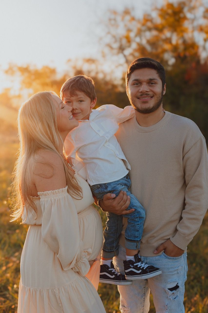 A family shares tender moments together in an autumn field at sunset.