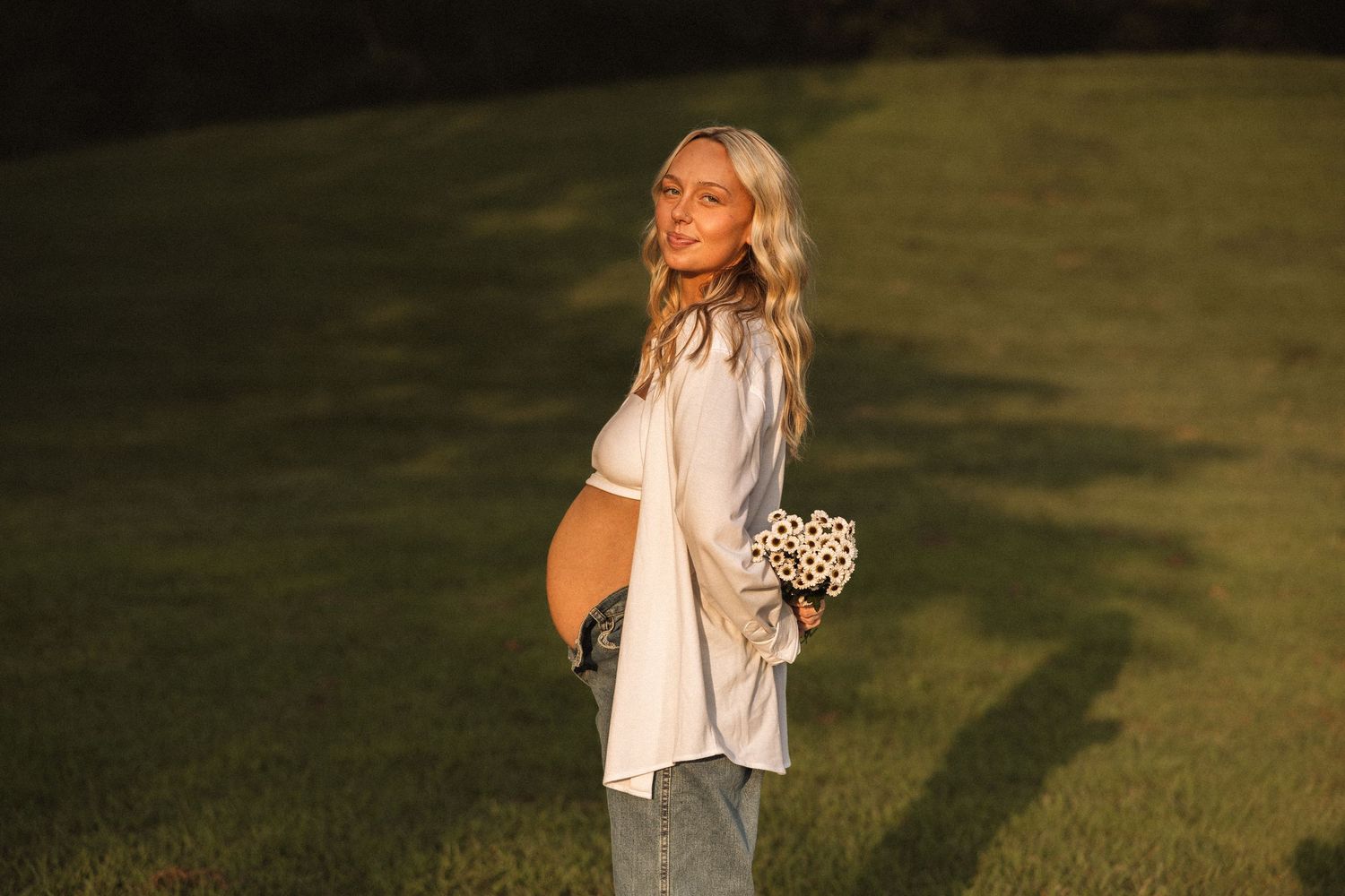 Golden hour maternity photoshoot in a grassy field with soft natural lighting.