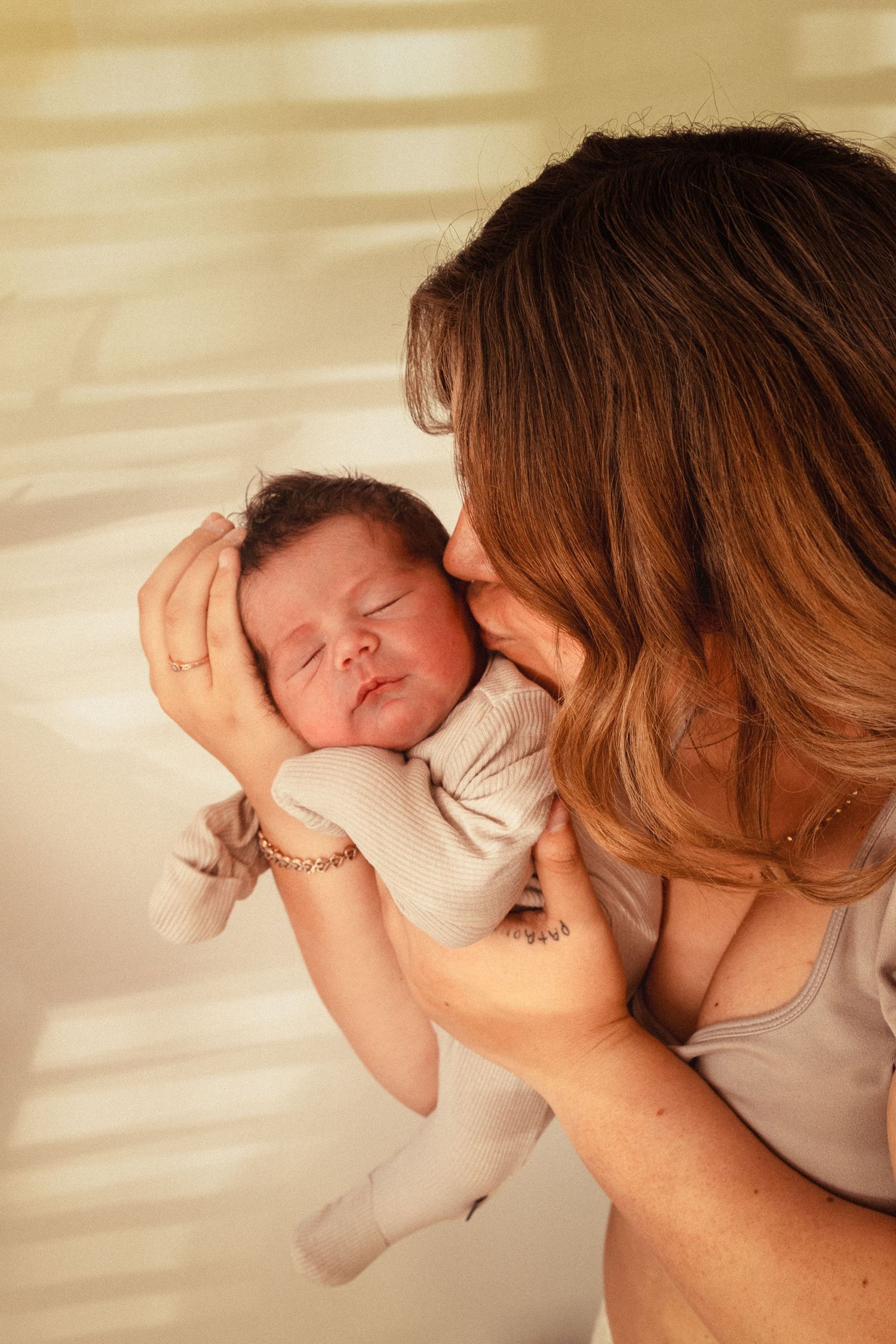 Tender newborn photography session with gentle natural window lighting casting shadows.