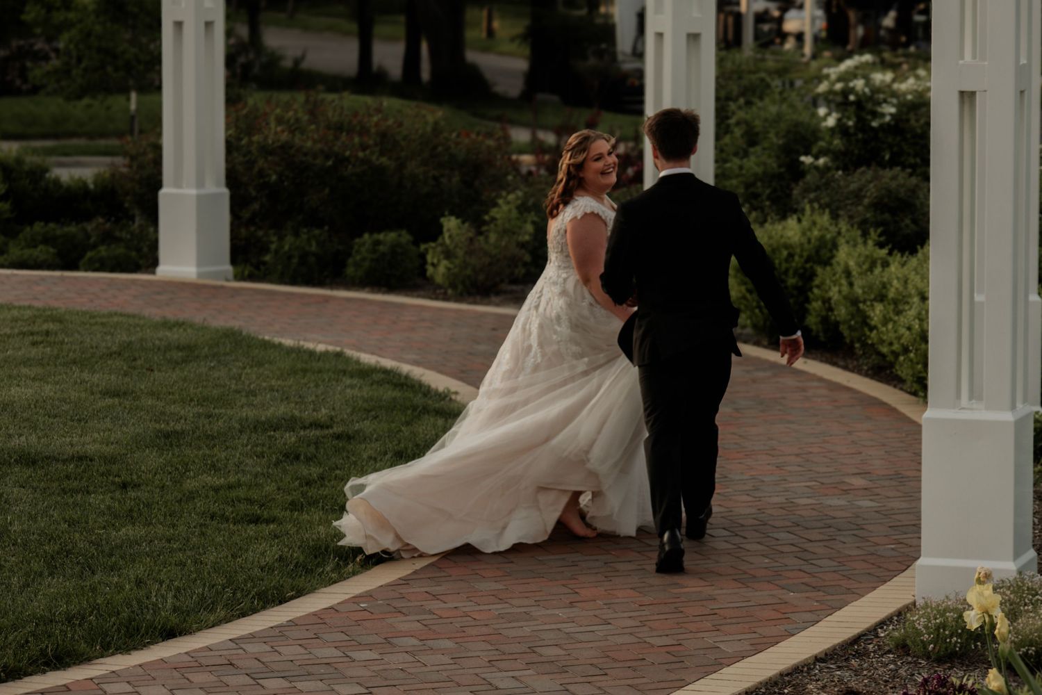 Wedding couple embraces near white colonial columns and brick pathway outdoors.