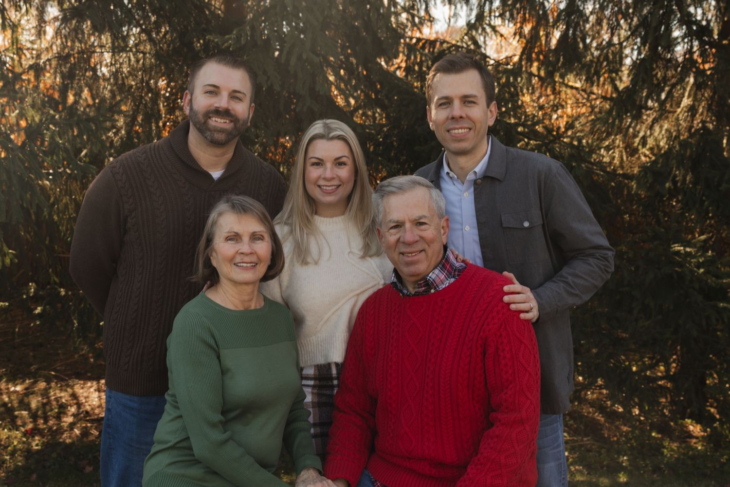 Family group poses together outdoors against autumn foliage during golden hour photo session.
