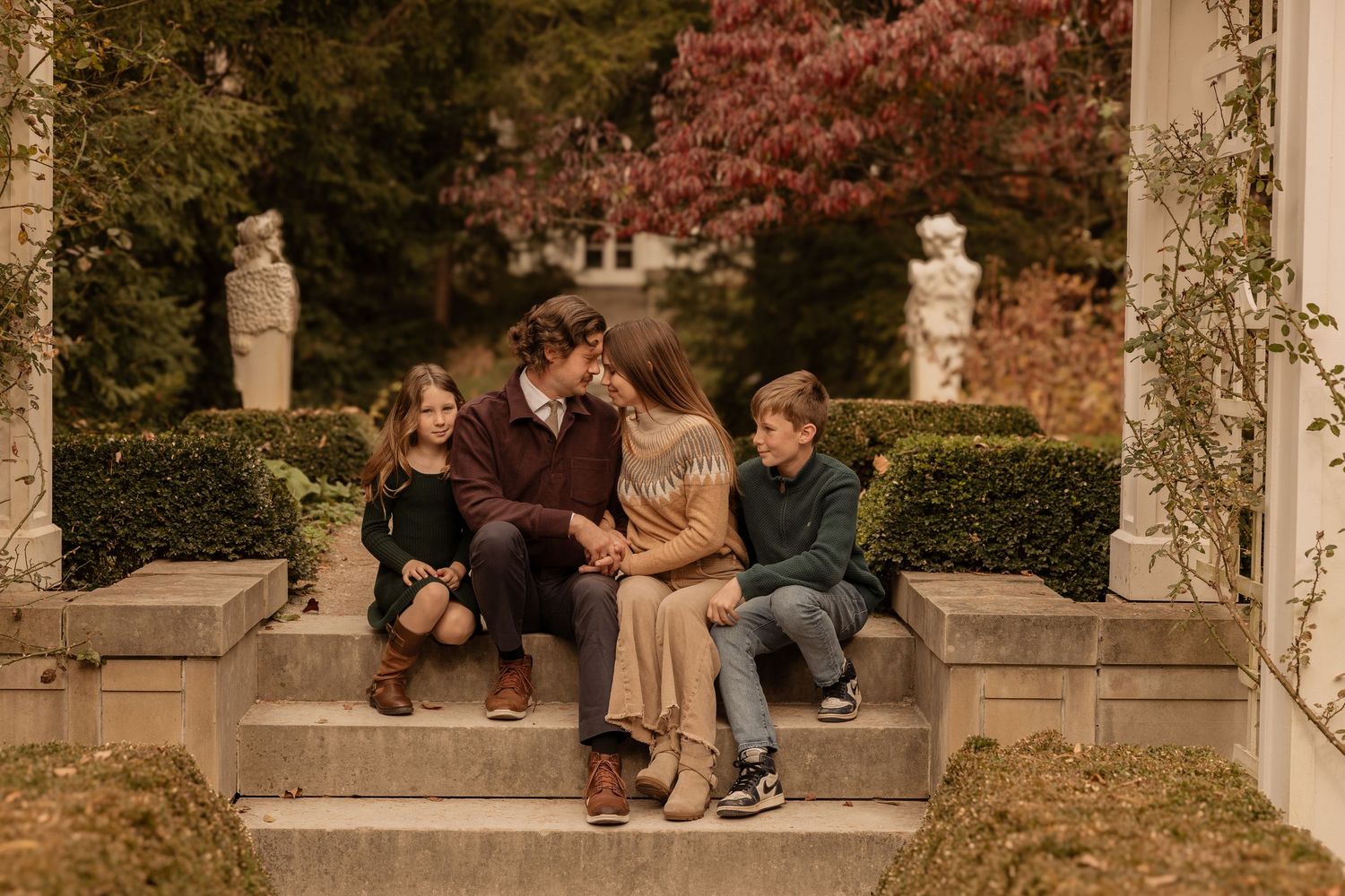 People sit and relax on stone steps in a garden gazebo during autumn with red foliage in the background.