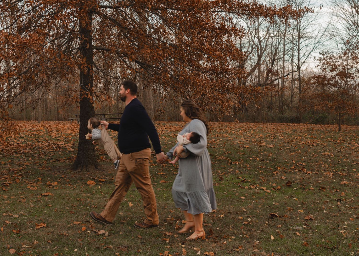 Family playfully running and walking through an autumn field at sunset.