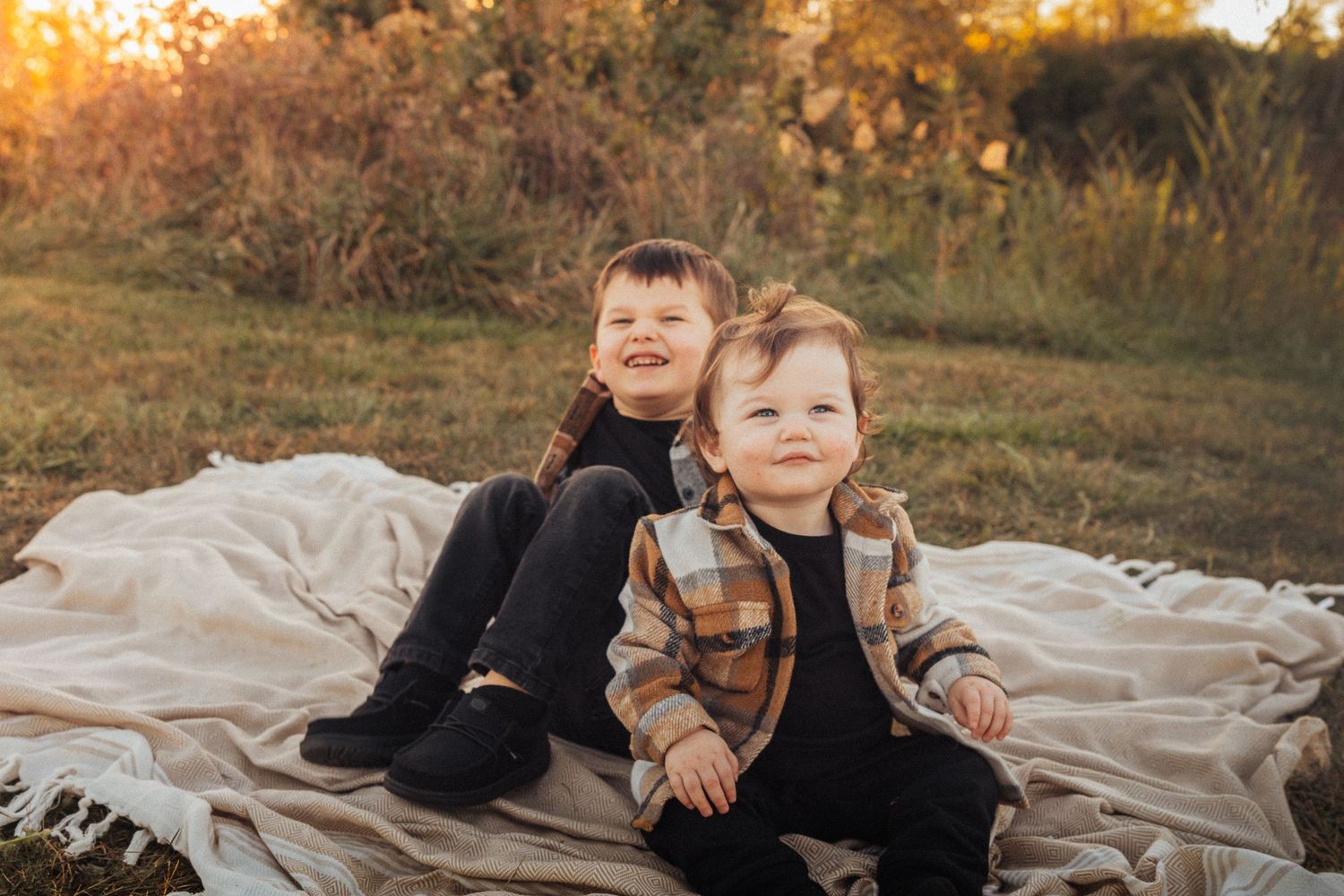 Family relaxing on blanket outdoors during golden hour autumn photoshoot.