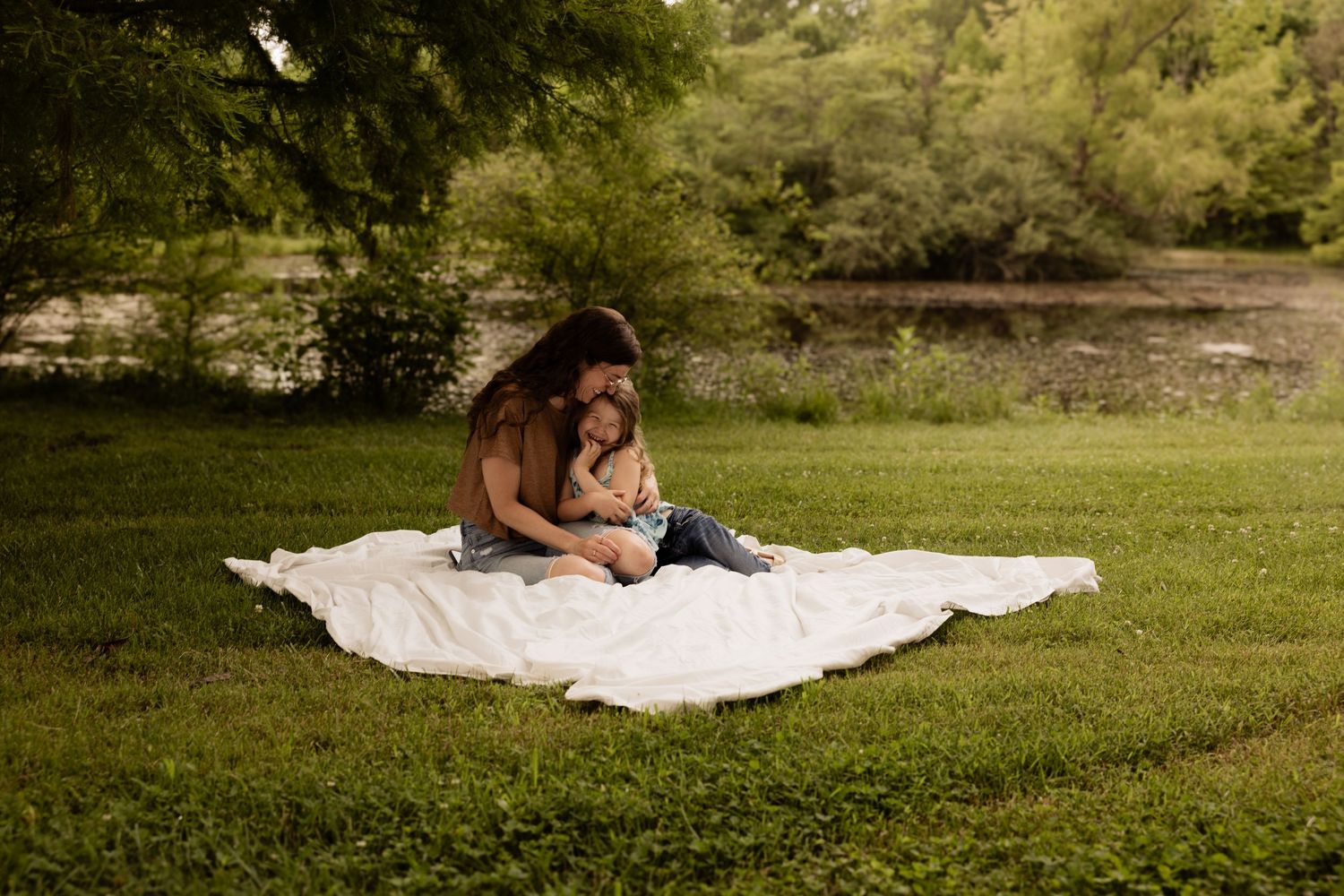Couple relaxing on white blanket spread out on grass during sunset photoshoot.