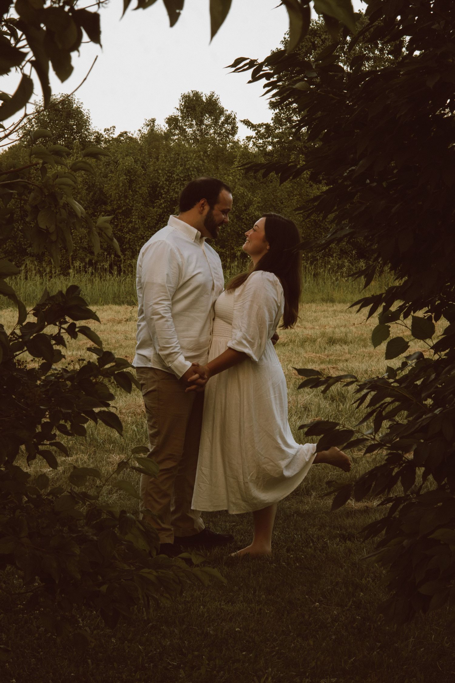 A romantic couple embraces on a serene path surrounded by lush greenery.