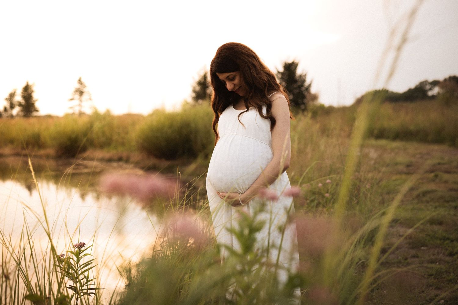 Lakeside maternity photography with tall grass and golden sunset light.