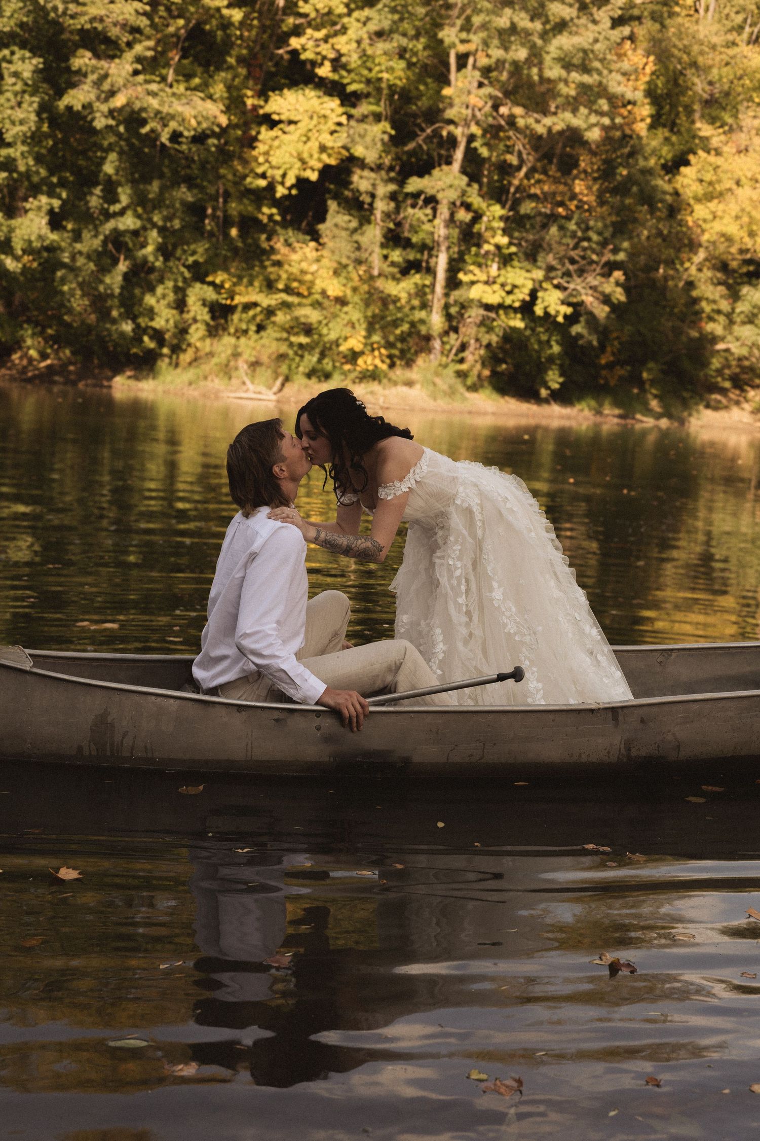 A couple sits intimately together on a wooden dock overlooking a tranquil autumn lake with golden foliage reflections.