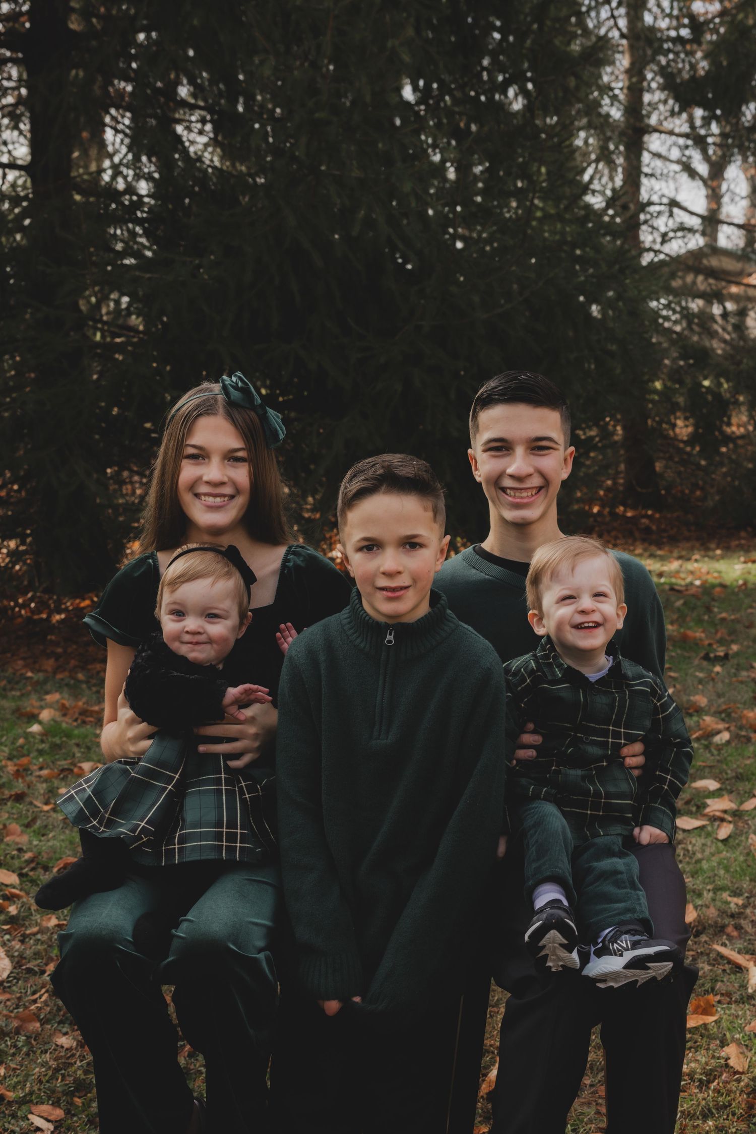 Group of children in coordinating dark outfits smile together during outdoor autumn photoshoot.