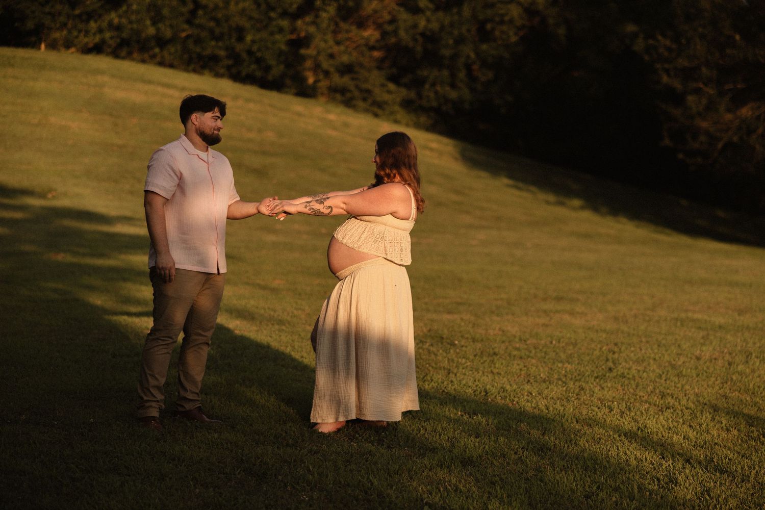 A loving couple walks hand in hand across a sunlit meadow at dusk.