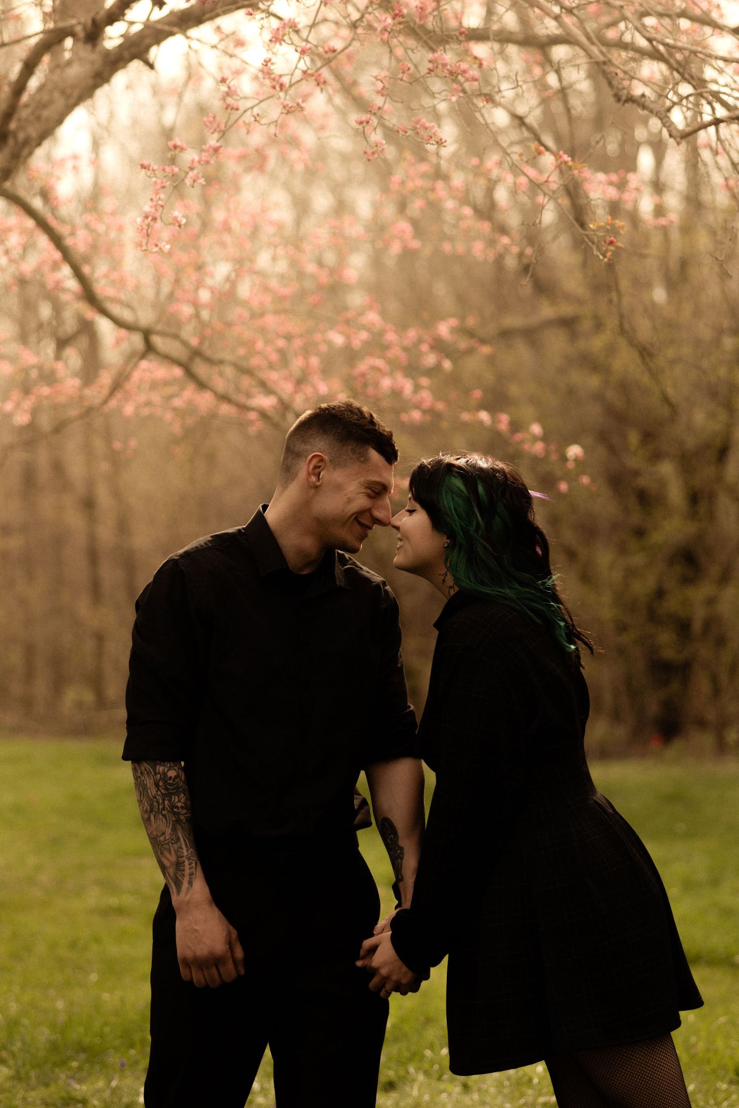 A couple in black attire shares tender moments against blooming spring trees.