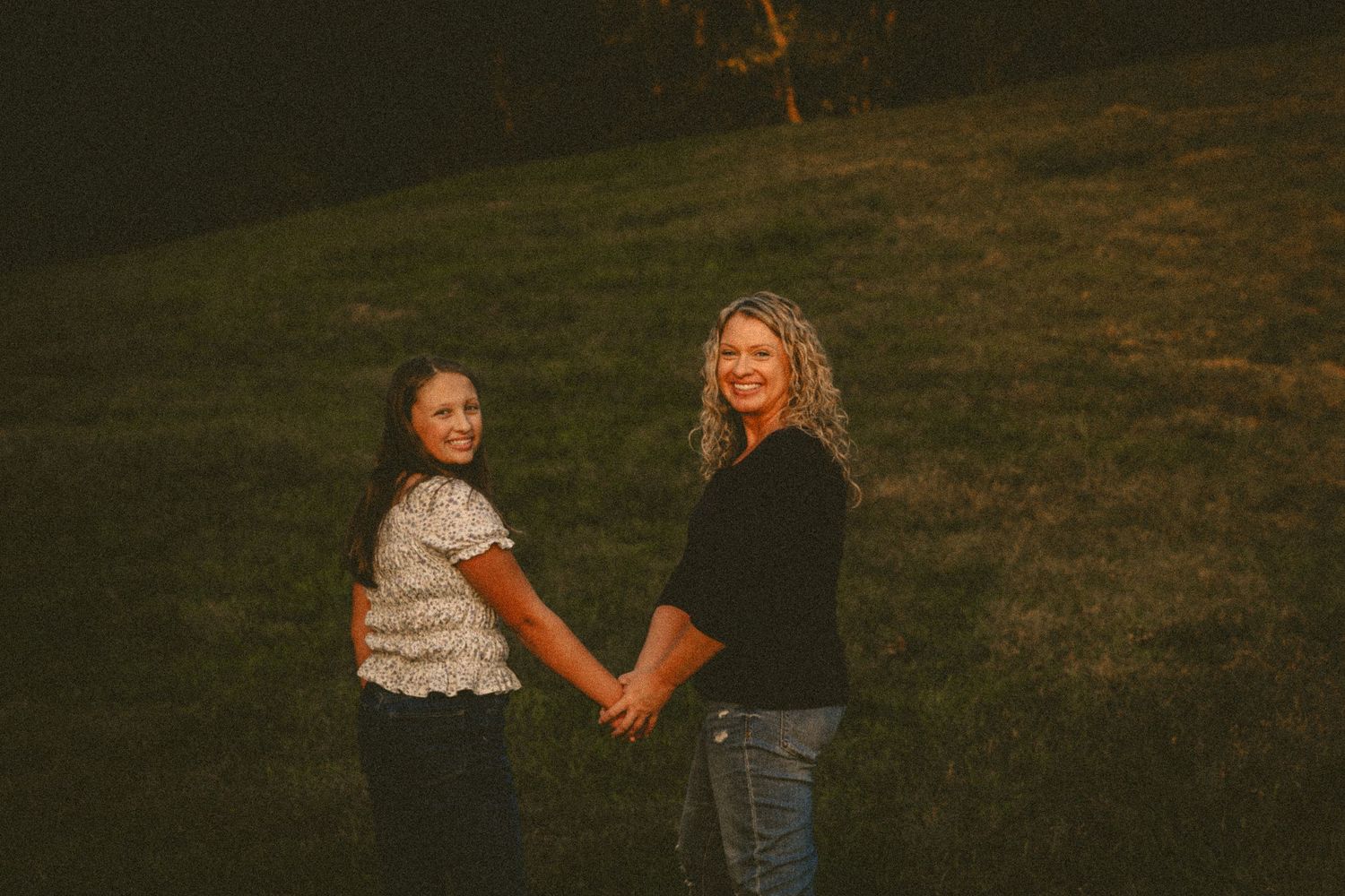 Two figures sitting together on grass at sunset in a casual outdoor photoshoot.