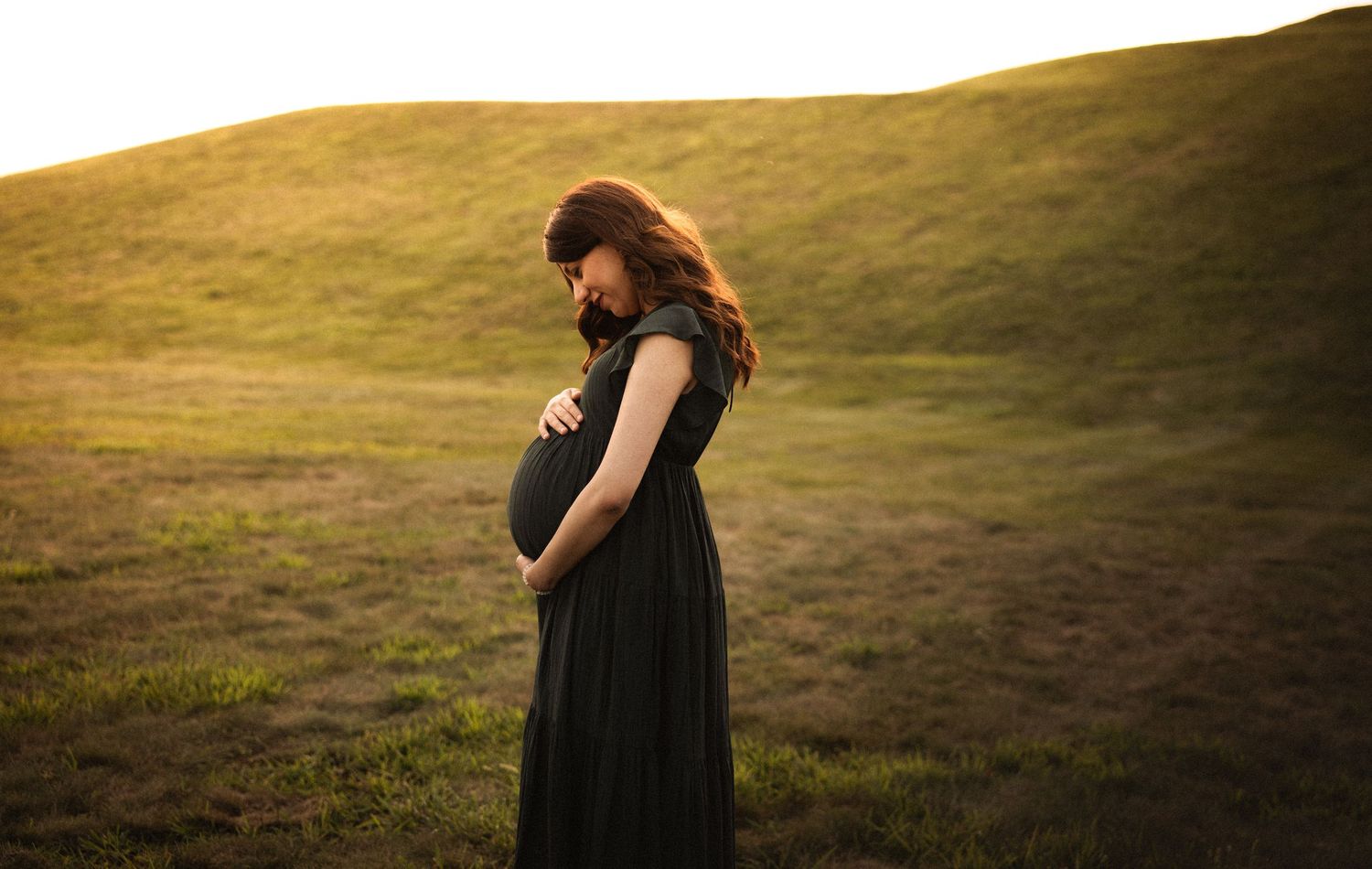 Sunset maternity photography session in a golden field with long shadows.