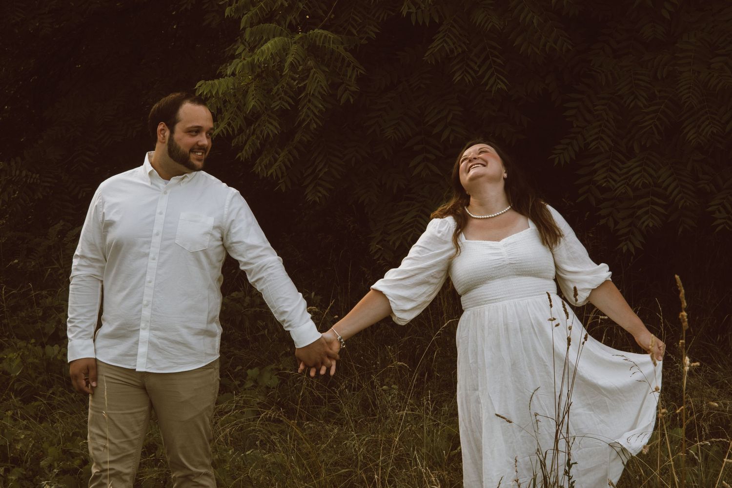 Two people in white outfits dance together in a romantic outdoor setting.