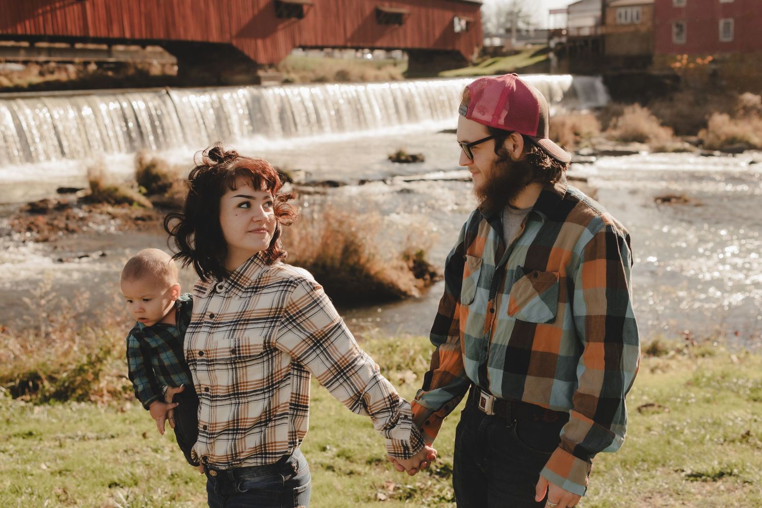 Family enjoying playful moments together by a rustic waterfall and red barn.