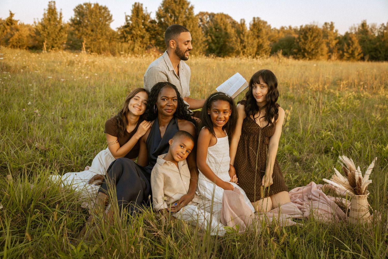 Family of six posing together in a sunlit green meadow during golden hour outdoor portrait session.