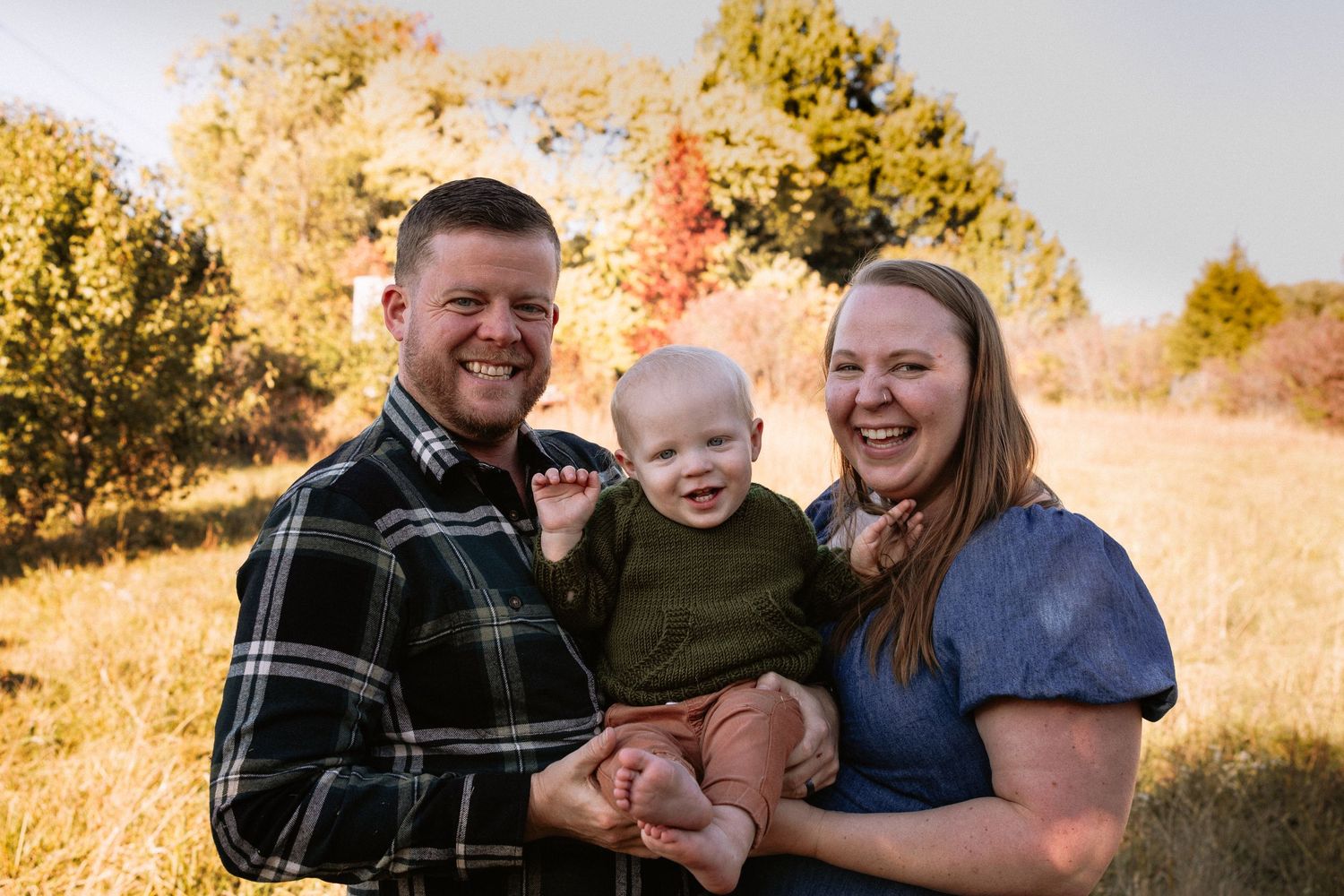 Family enjoying outdoor autumn photoshoot with golden sunlight and natural scenery.