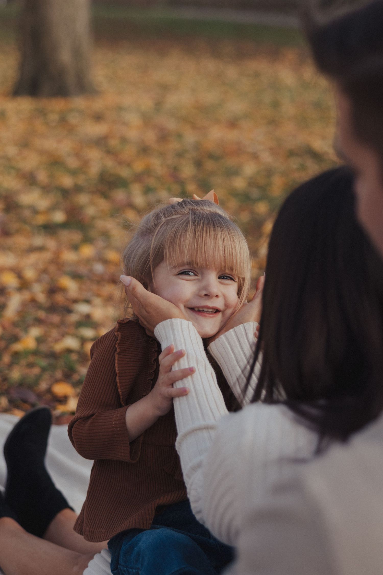Playful child in brown coat making silly faces during outdoor family photoshoot.