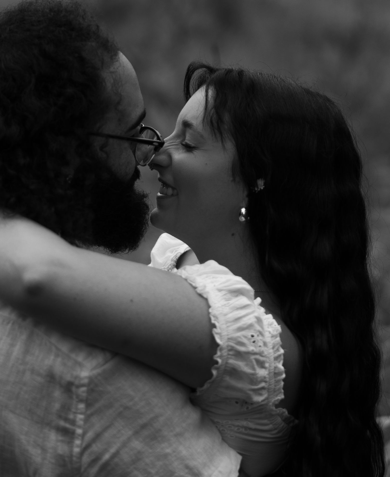 Black and white photo of a couple sharing a romantic moment, smiling and about to kiss in an outdoor setting.