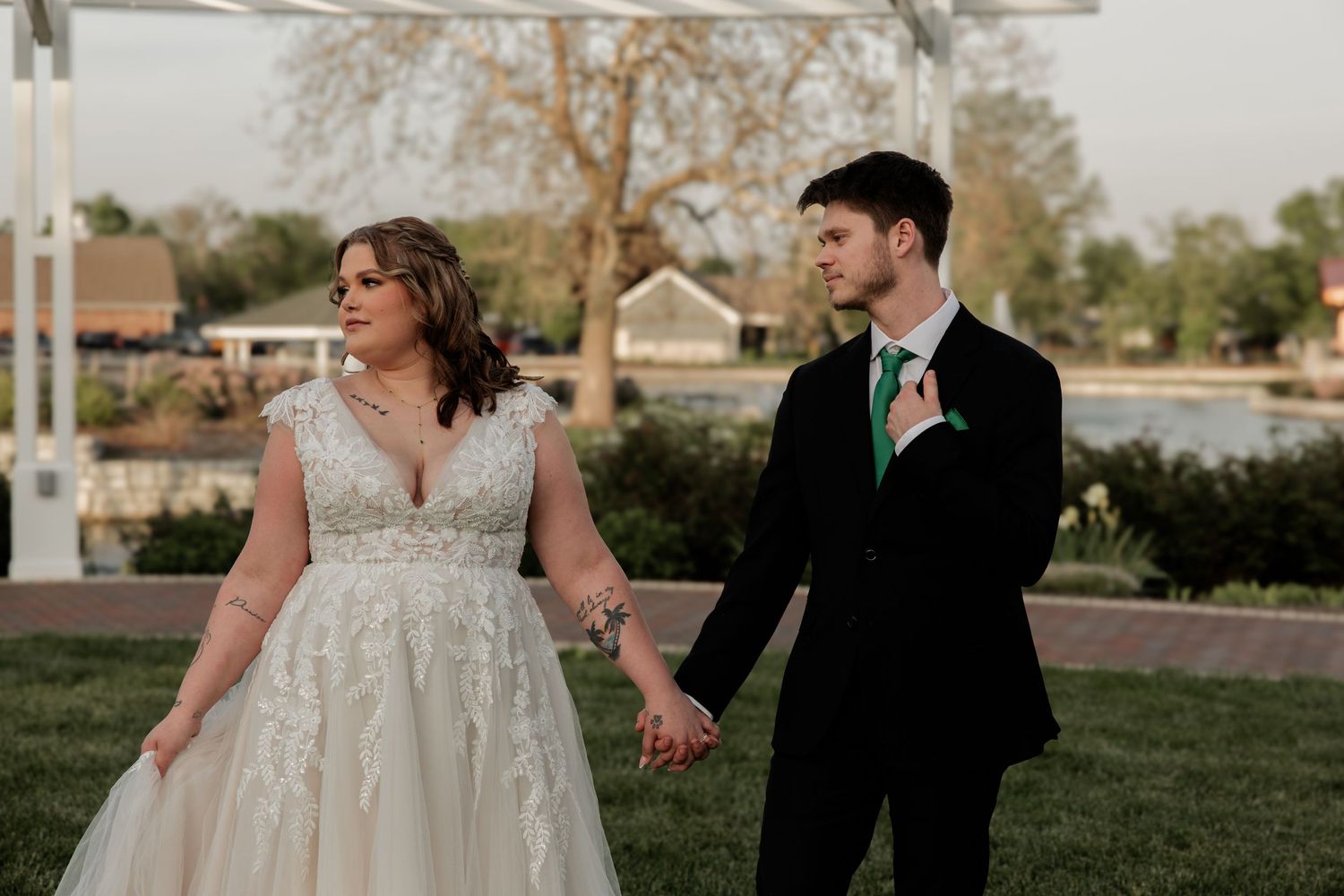 Wedding couple shares candid moment on lawn with architectural elements in background.