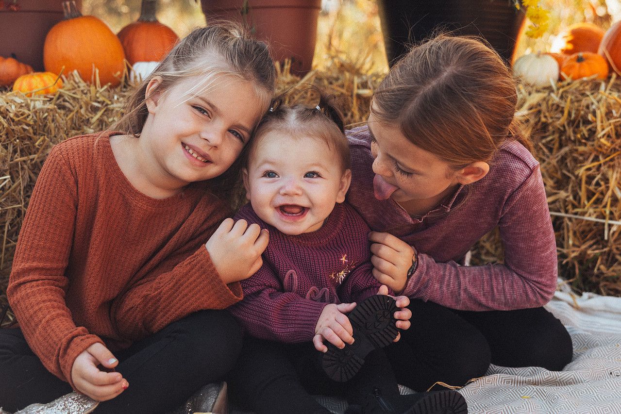 People sitting in an autumn scene with hay bales and pumpkins, sharing warm moments outdoors on a fall day.