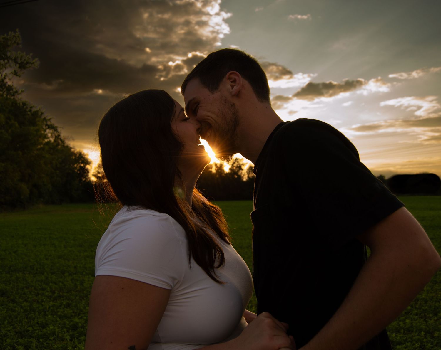 Silhouettes of a couple share an intimate moment against a dramatic sunset sky.