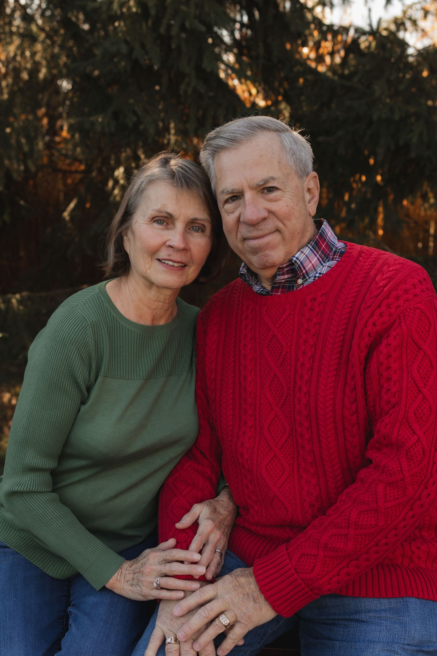Mature couple in red and green sweaters sharing intimate moments outdoors.