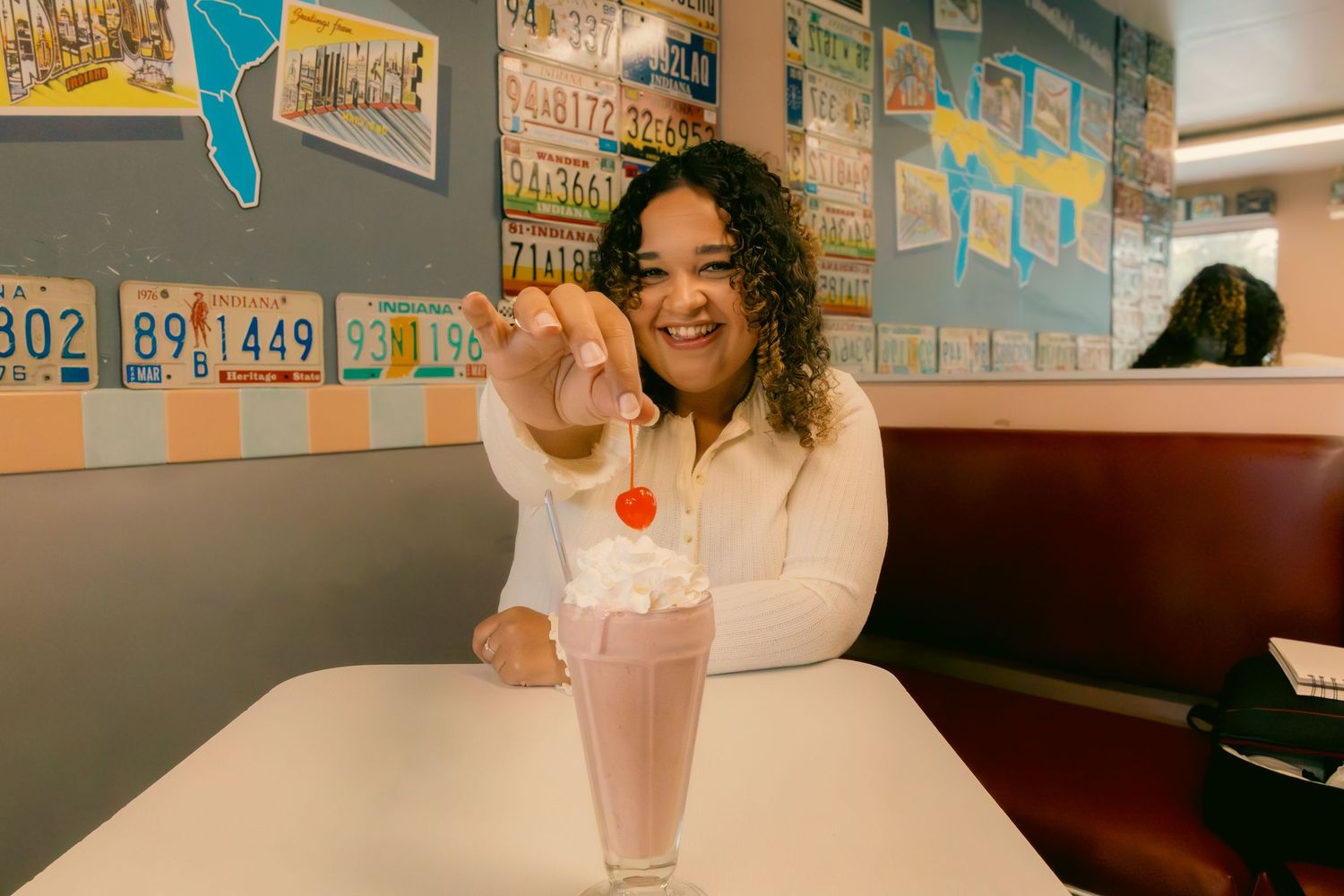 Person enjoying a milkshake at a retro diner with vintage posters on wall.
