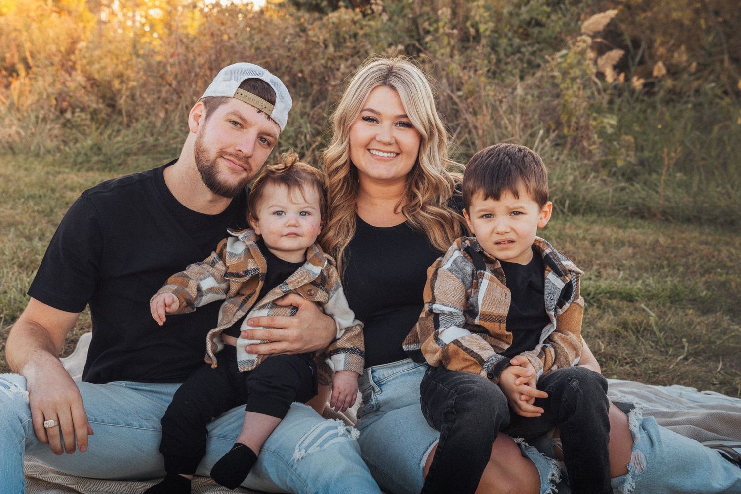 Family group sitting together on ground during autumn sunset photoshoot.
