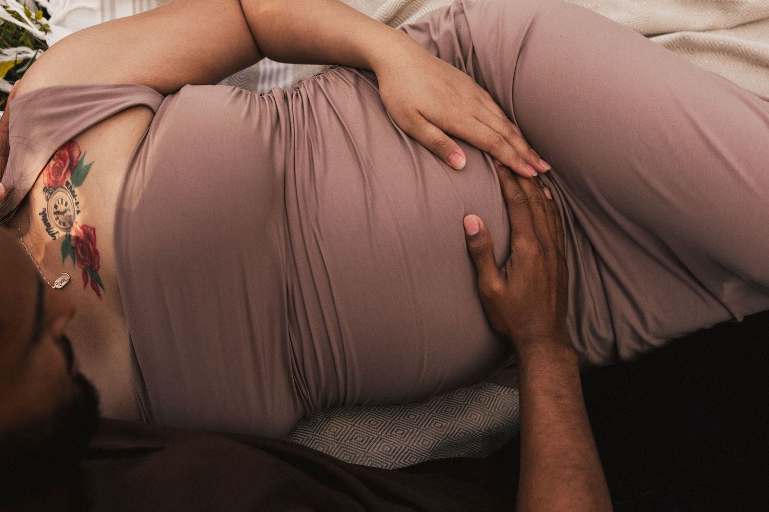 Close up of hands tenderly touching maternity dress in natural light.