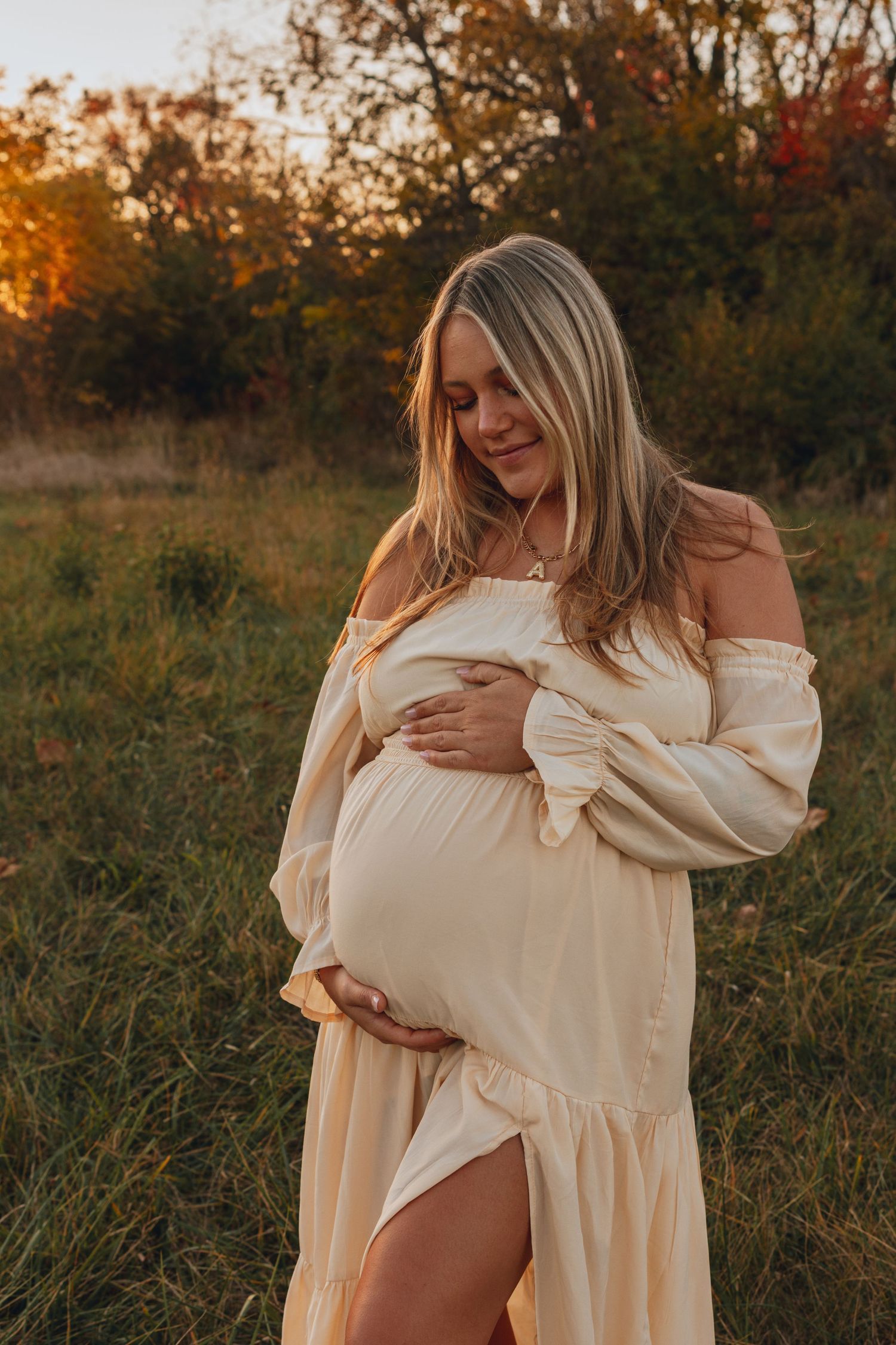 A woman in a white dress cradles her belly during a sunset maternity photoshoot.