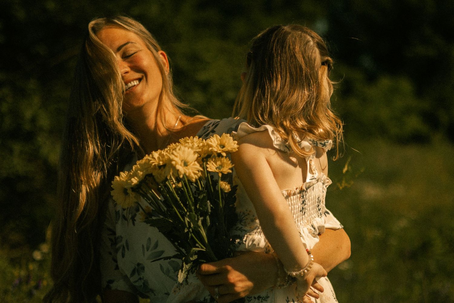 Two people in white dresses twirling together among wildflowers at golden hour.