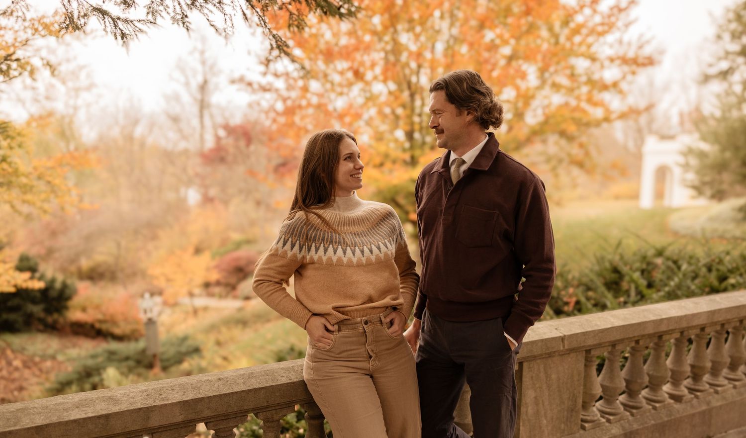 A couple walks together through a park filled with vibrant autumn foliage on a romantic fall afternoon.