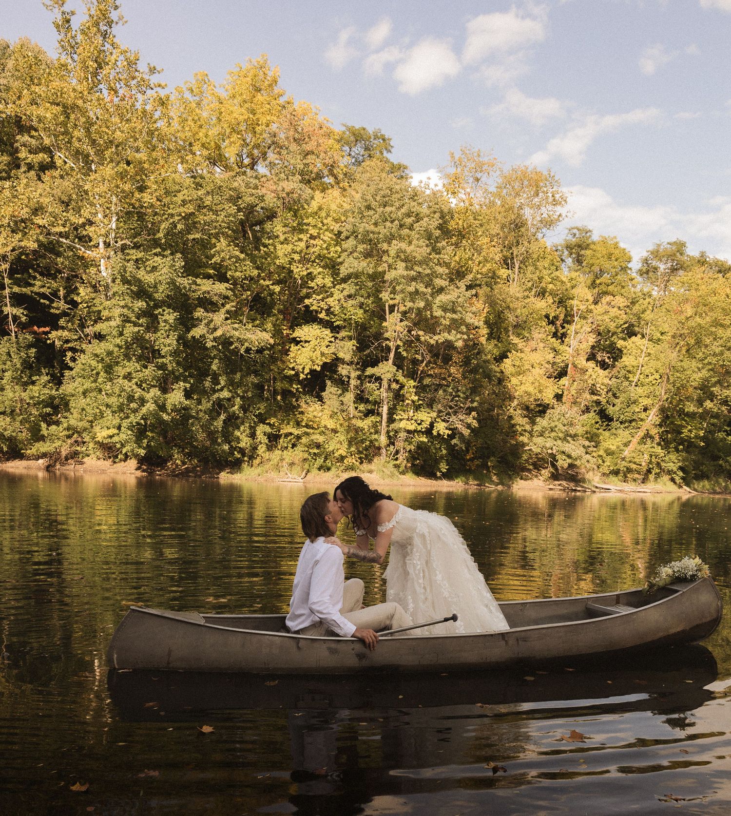 Two people enjoying a romantic canoe ride on a tranquil lake surrounded by autumn trees with golden foliage.