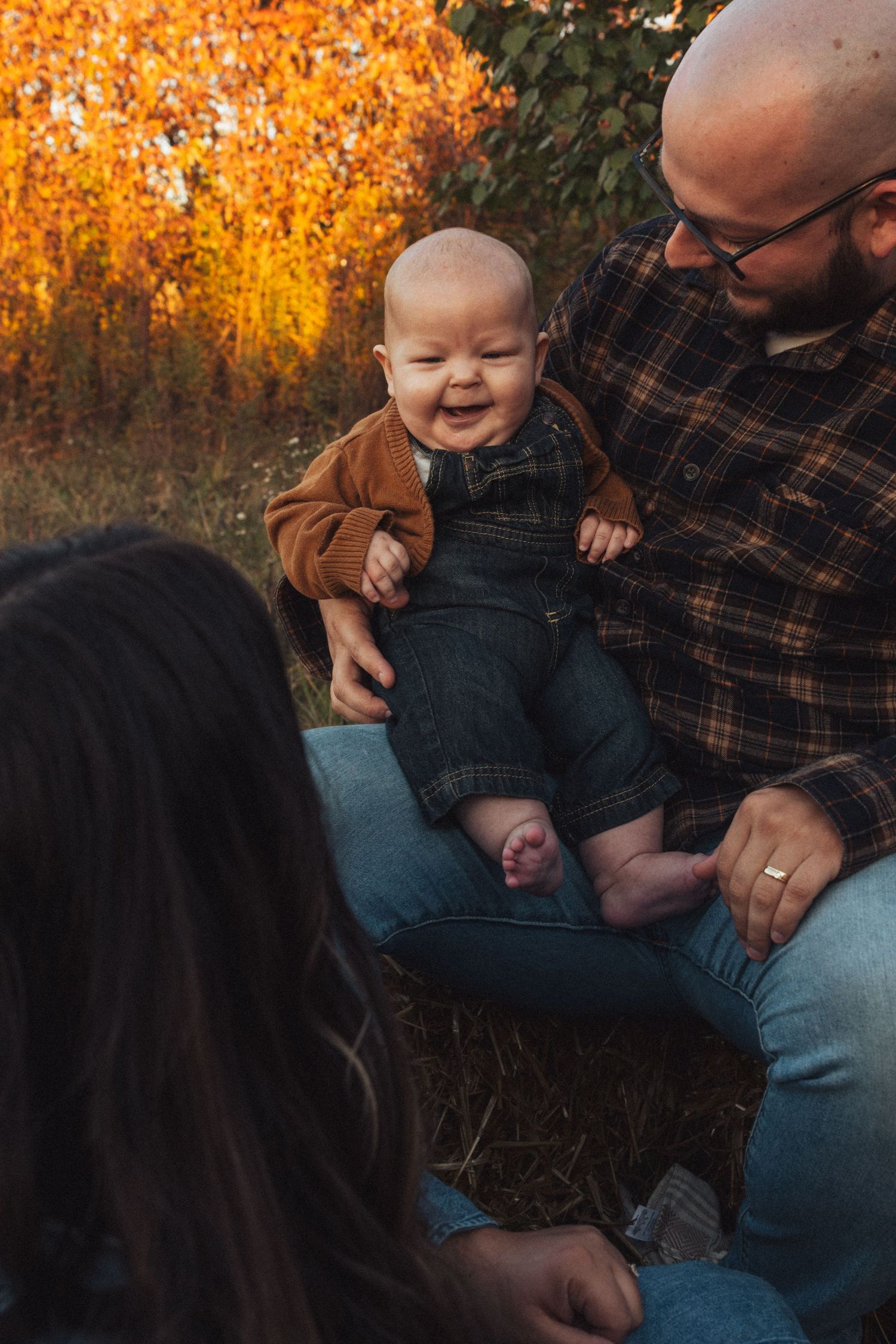 Family sitting together on blanket during autumn sunset with golden foliage backdrop.